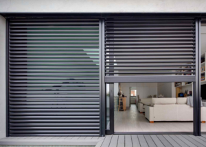 Volets roulants gris foncés sur grande baie vitrée donnant sur une terrasse et un intérieur moderne.