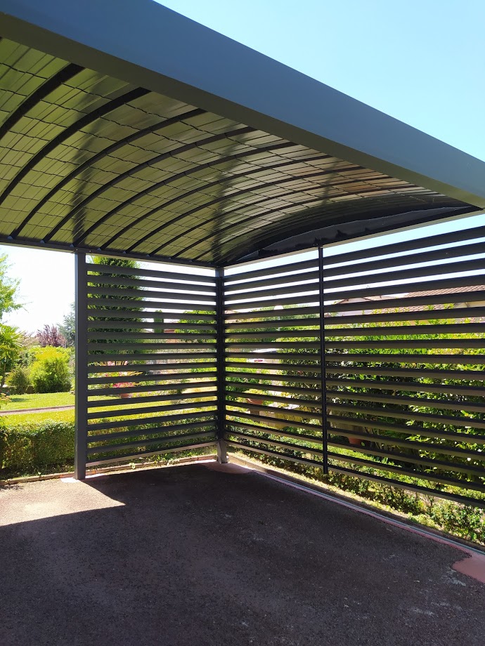 Carport moderne gris foncé avec toit incurvé en polycarbonate et côtés à lames, offrant de l'ombre sur une allée.