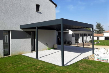 Pergola bioclimatique moderne gris anthracite adossée à une maison, couvrant une terrasse en gravier blanc.