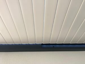 Toit de pergola blanc à lames parallèles légèrement ouvertes. Poutre gris foncé avec éclairage LED. Mur blanc texturé.