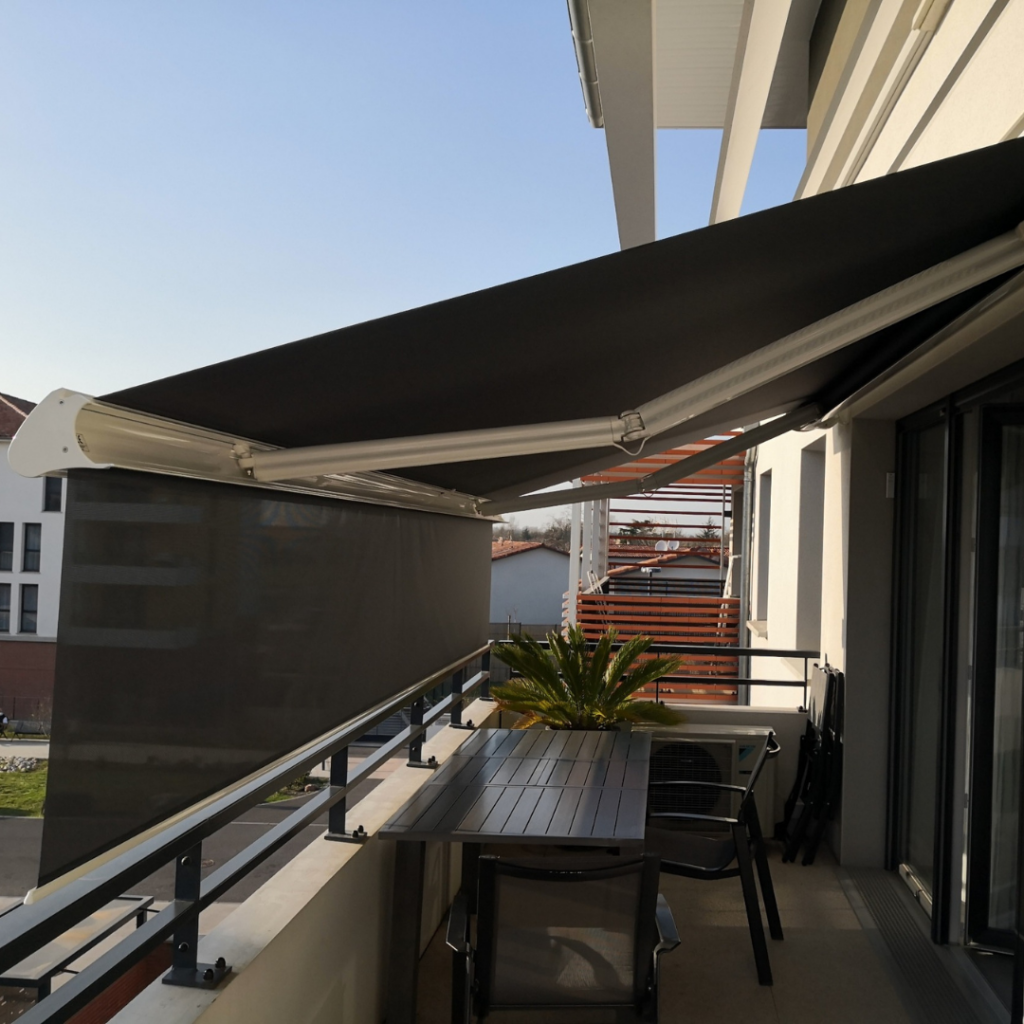 Balcon moderne avec grand store banne noir déployé au-dessus d'une table, chaises et plante sous ciel bleu clair.