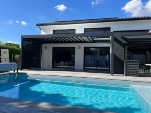 Maison moderne blanche avec piscine bleue, pergola bioclimatique noire sur terrasse, jardin ensoleillé.