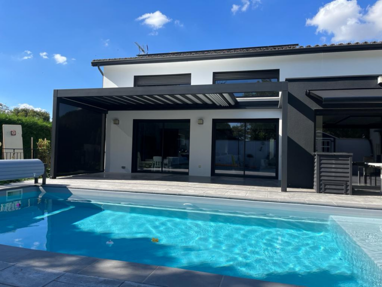 Maison moderne blanche avec piscine bleue, pergola bioclimatique noire sur terrasse, jardin ensoleillé.