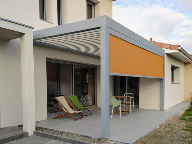 Pergola moderne grise avec lames orientables et store latéral orange, couvrant une terrasse carrelée devant une maison.