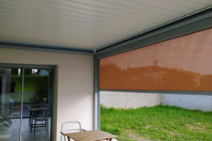 Terrasse couverte avec store extérieur orange baissé, protégeant du soleil et créant un espace ombragé près du jardin.