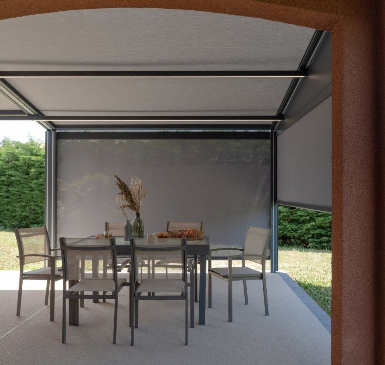 Salon de jardin sous une pergola bioclimatique moderne avec stores latéraux gris rétractables et éclairage LED intégré.