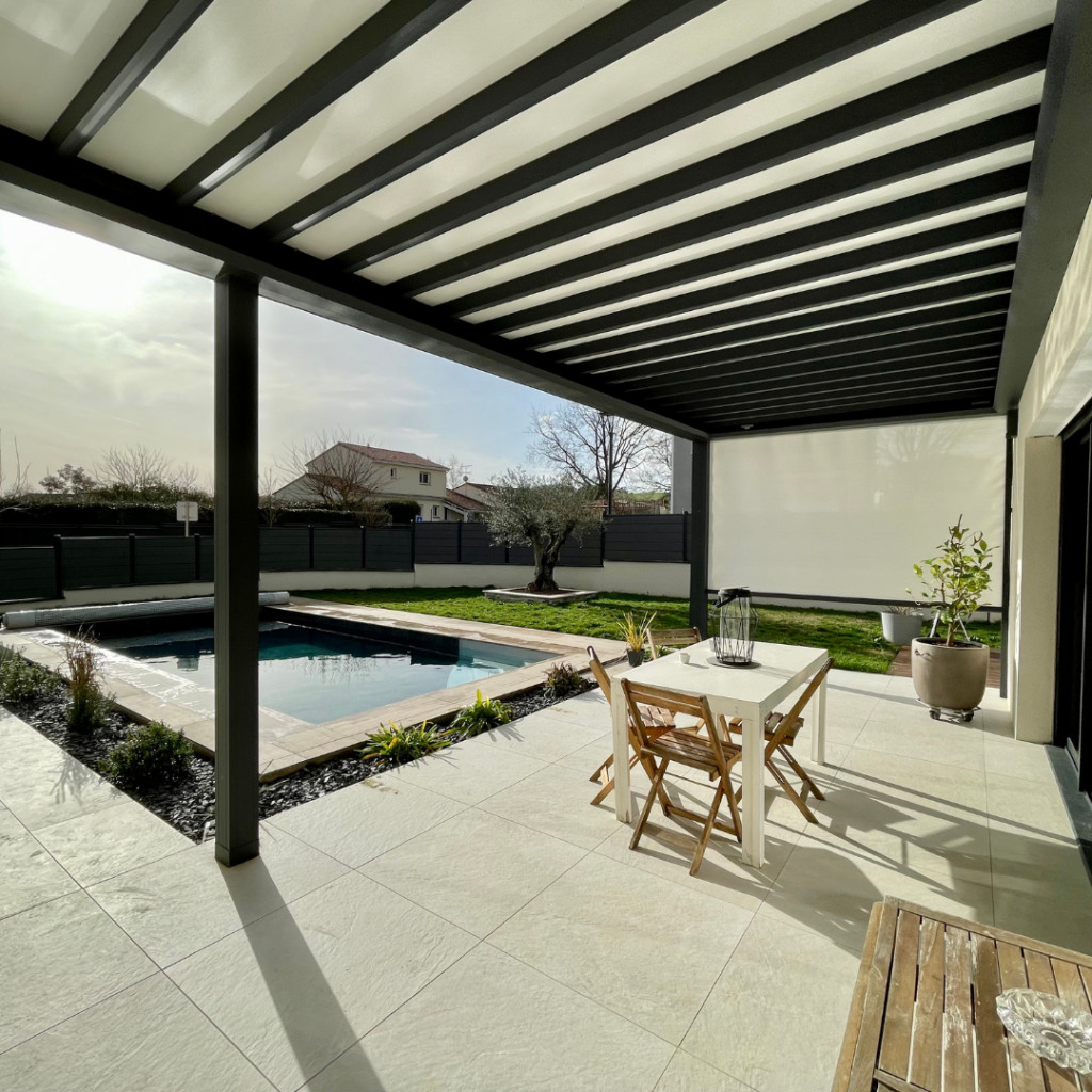 Patio moderne avec pergola bioclimatique, piscine, carrelage clair et jardin. Table et chaises sur la terrasse ensoleillée.