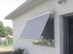 Store banne gris moderne déployé sur une fenêtre de façade de maison blanche, protégeant du soleil.