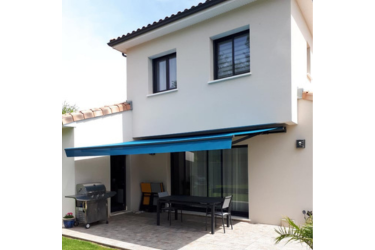 Store banne bleu sur terrasse de maison, offrant de l'ombre et protection solaire. Salon de jardin, table et barbecue.
