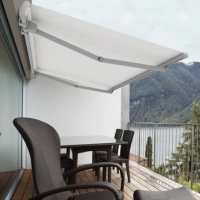 Store banne blanc retractable sur balcon avec table et chaises, vue magnifique sur lac et montagnes.