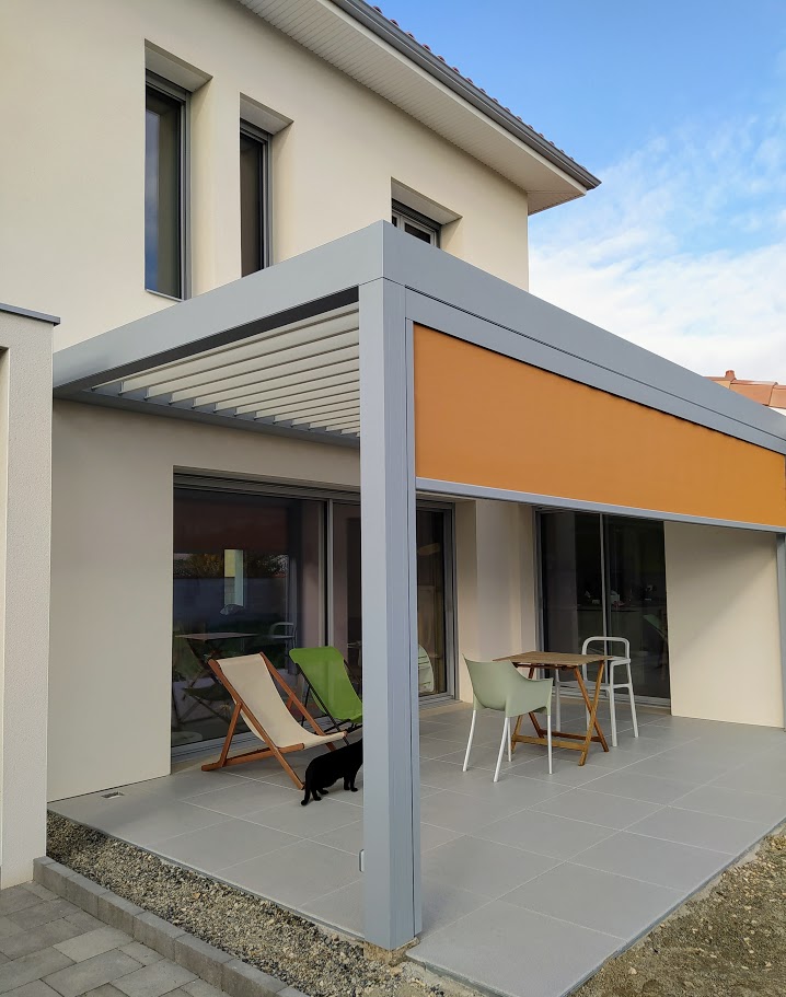 Terrasse moderne avec pergola bioclimatique grise, store latéral orange, mobilier extérieur et chat noir.