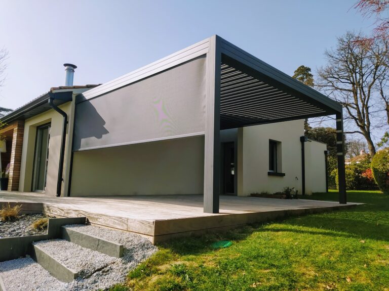 Maison avec terrasse bois, pergola bioclimatique anthracite, store vertical. Jardin ensoleillé.