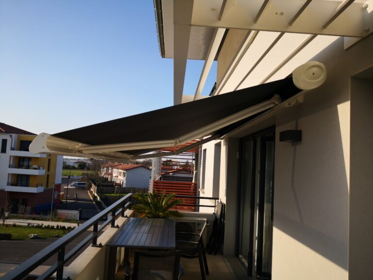 Store banne noir déployé sur un balcon avec table et chaises, vue sur la ville par beau temps.