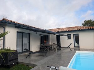 Terrasse moderne avec store banne déployé, mobilier d'extérieur, et piscine sous un ciel nuageux.
