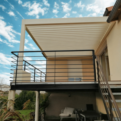 Balcon en acier noir soutenu par des poteaux, surmonté d'une pergola bioclimatique beige. Garde-corps minimaliste et escalier extérieur.