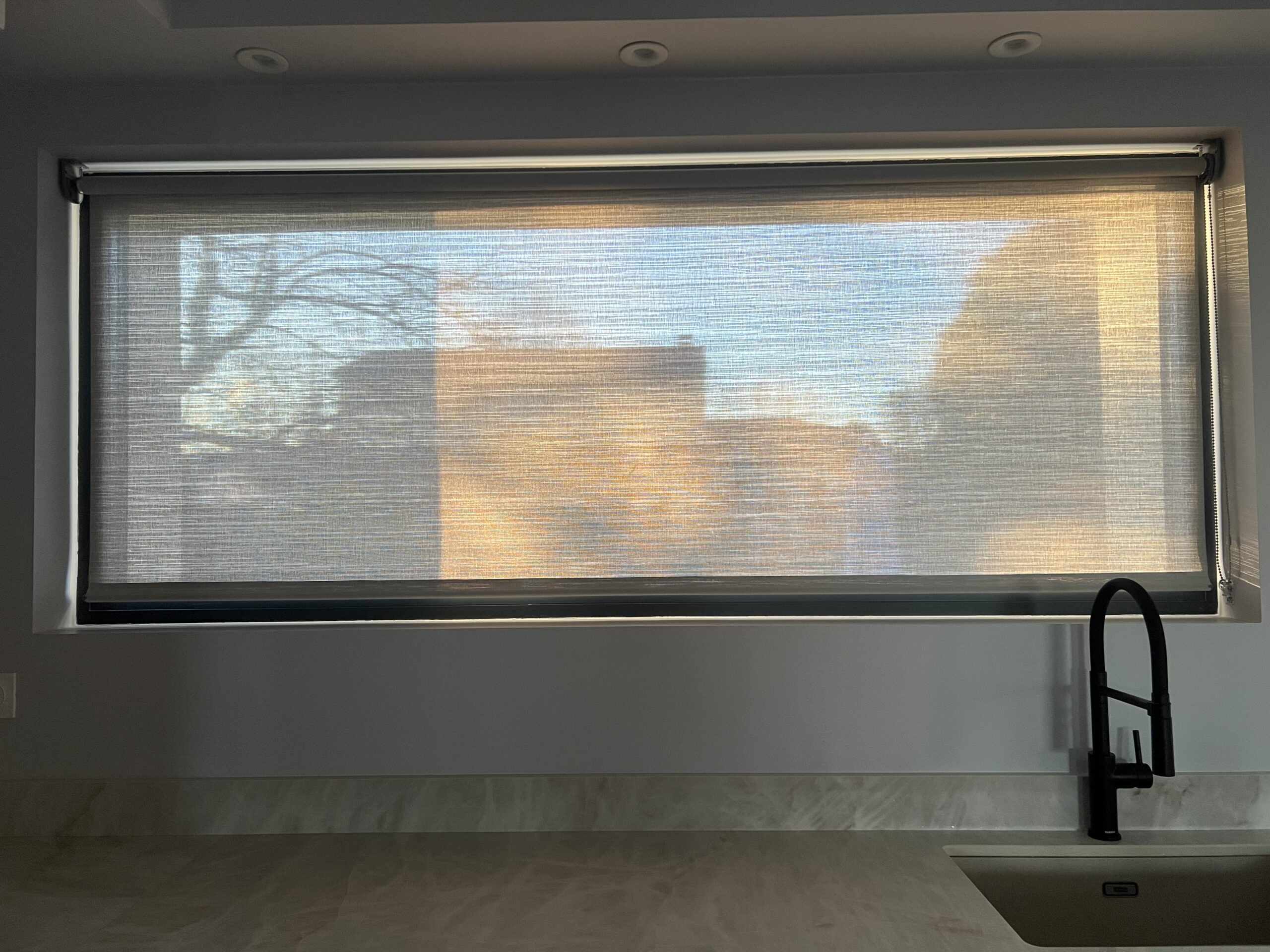 Store enrouleur fermé filtrant la lumière chaude du soleil dans une cuisine.