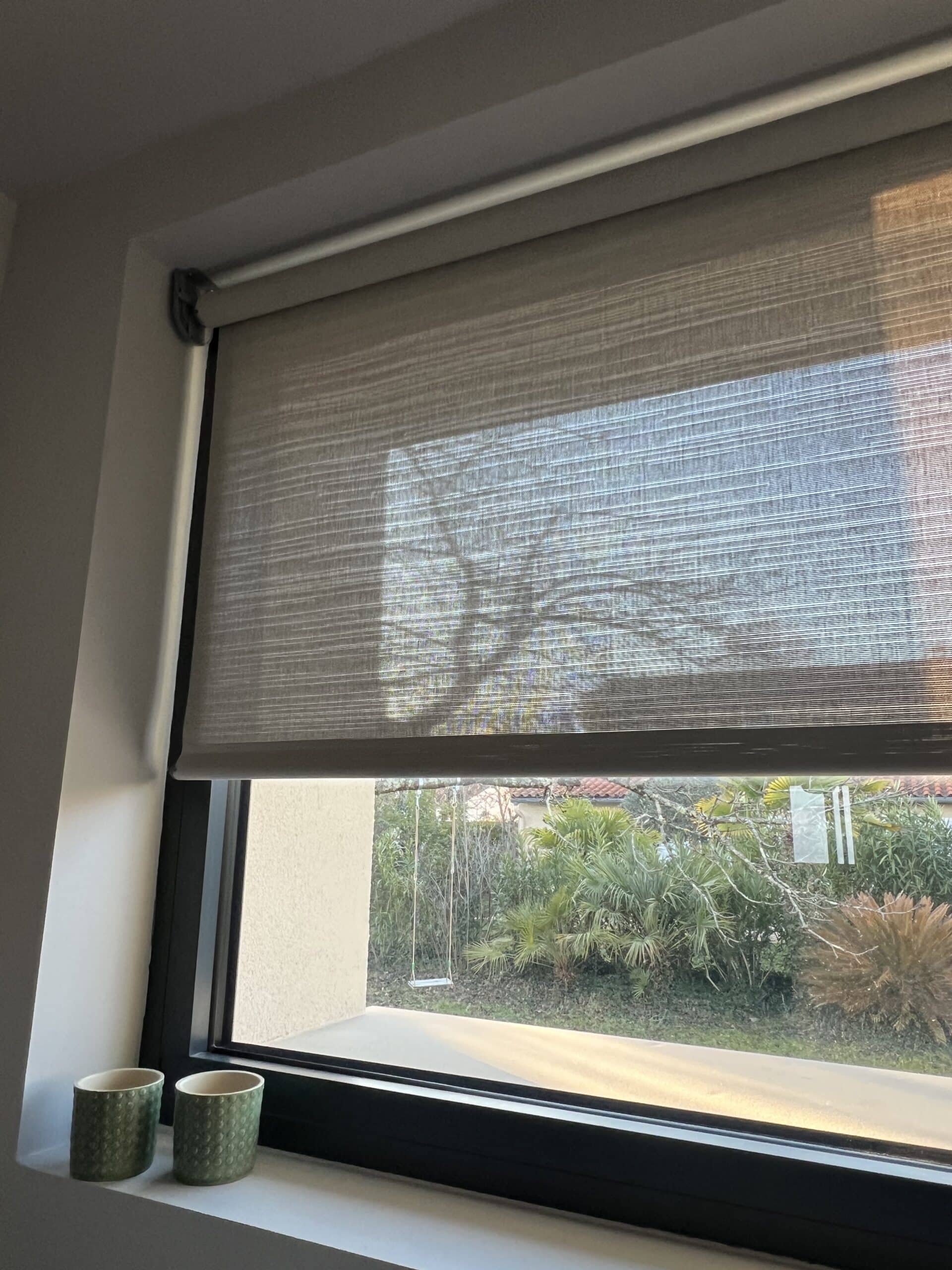 Store enrouleur moderne filtrant la lumière du soleil sur une fenêtre.