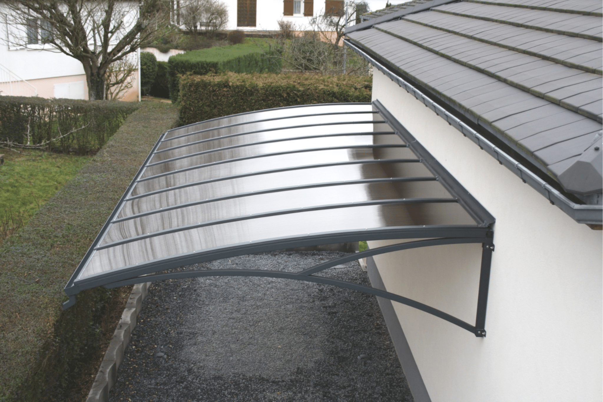 Abri de voiture mural en polycarbonate fumé et aluminium gris anthracite fixé sur la façade d'une maison.