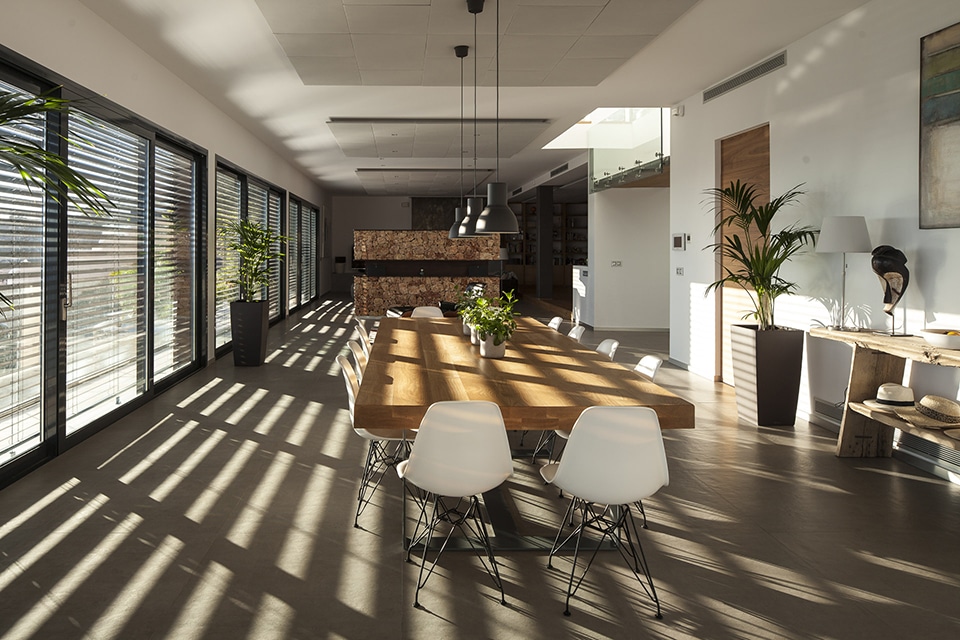 Salle à manger design avec table en bois massif, chaises blanches et jeux d'ombres à travers les brise-soleils Aluflex.
