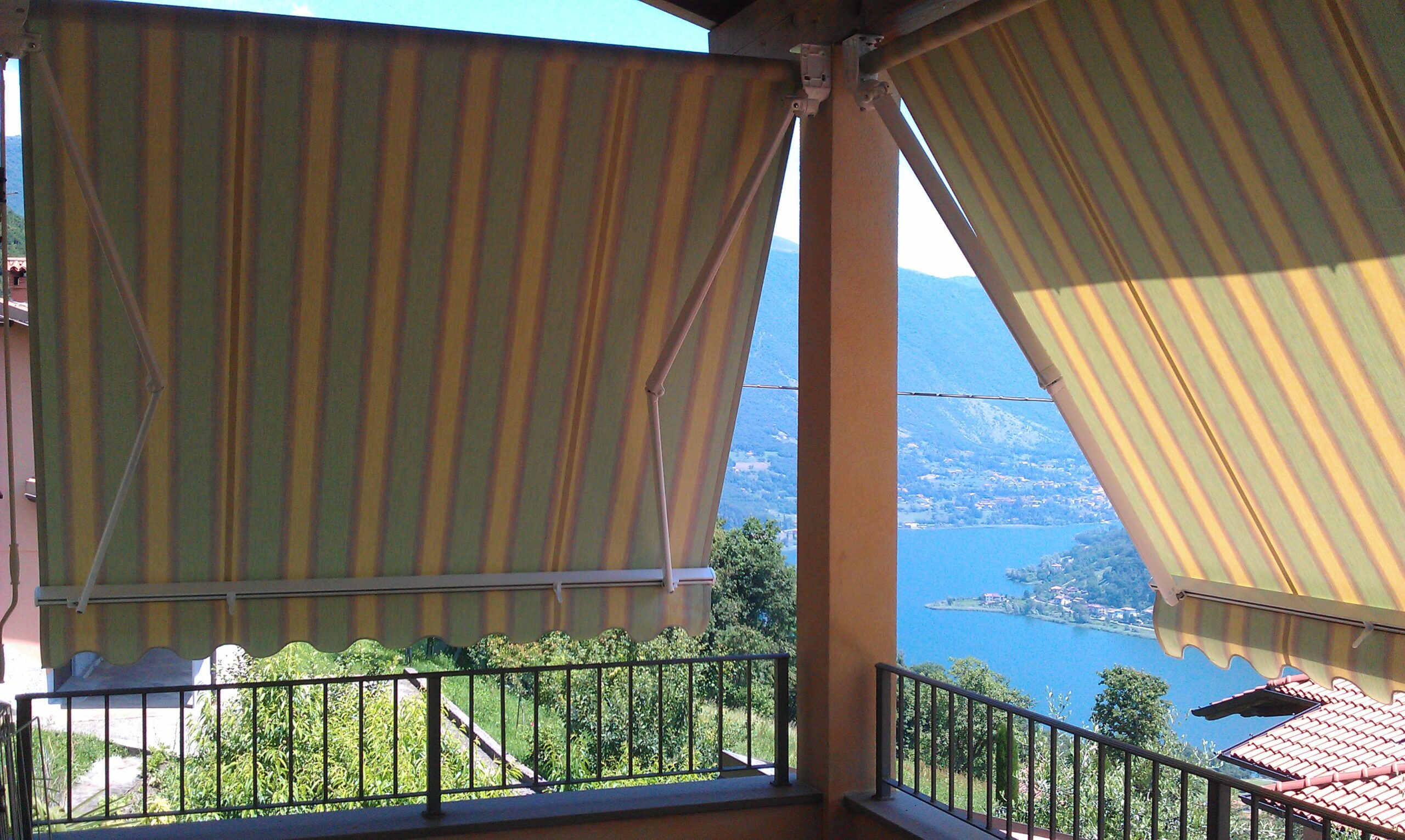 Store banne rayé sur balcon offrant une vue panoramique sur un lac et les montagnes par temps clair.