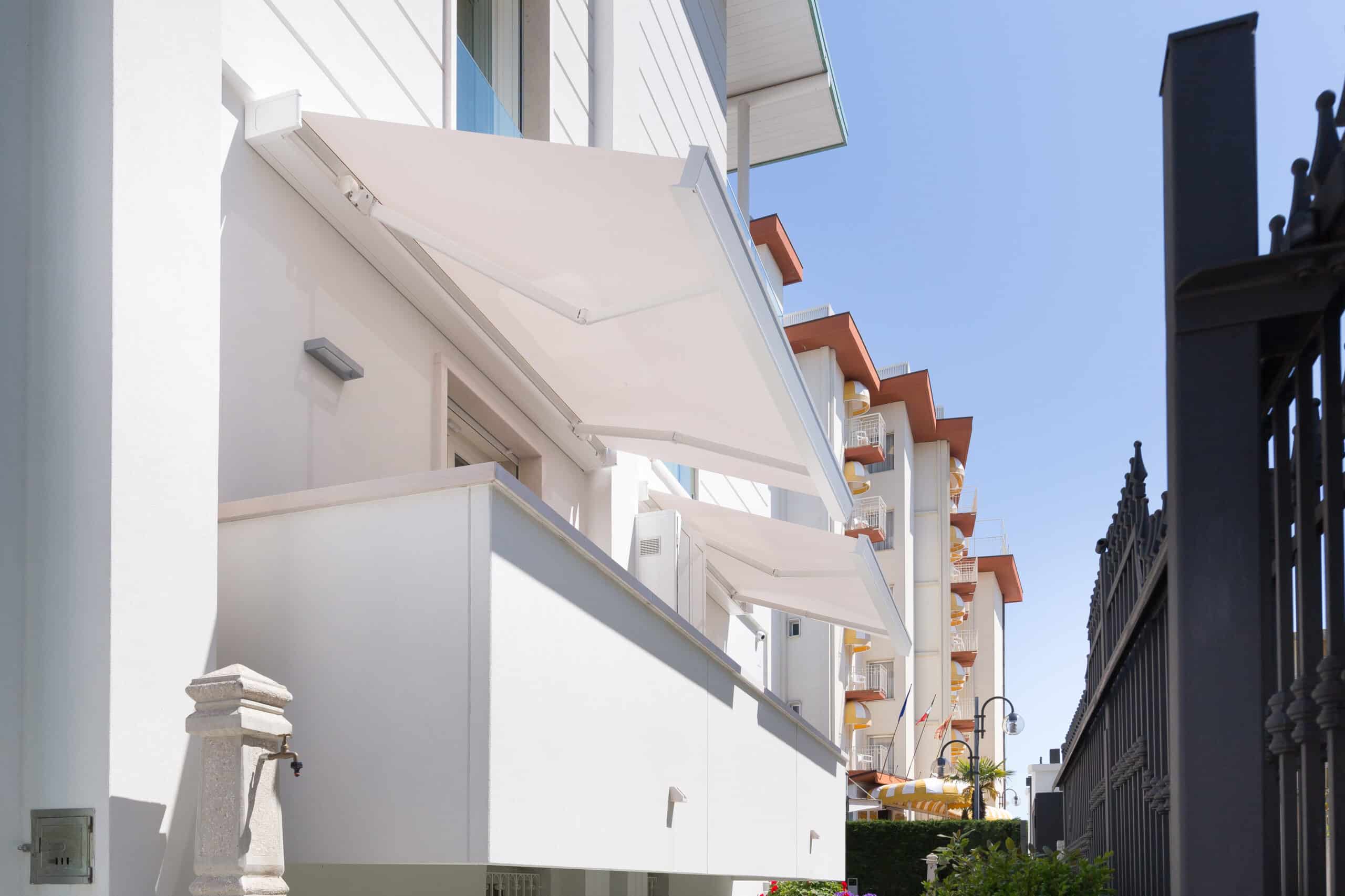 Store banne blanc rétractable sur le balcon d'un immeuble moderne sous un ciel bleu dégagé.