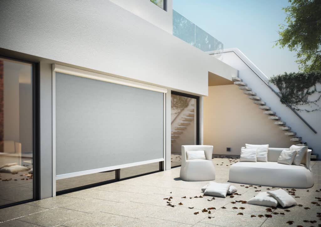 Store vertical extérieur gris sur terrasse de villa moderne avec salon de jardin blanc et escalier extérieur.