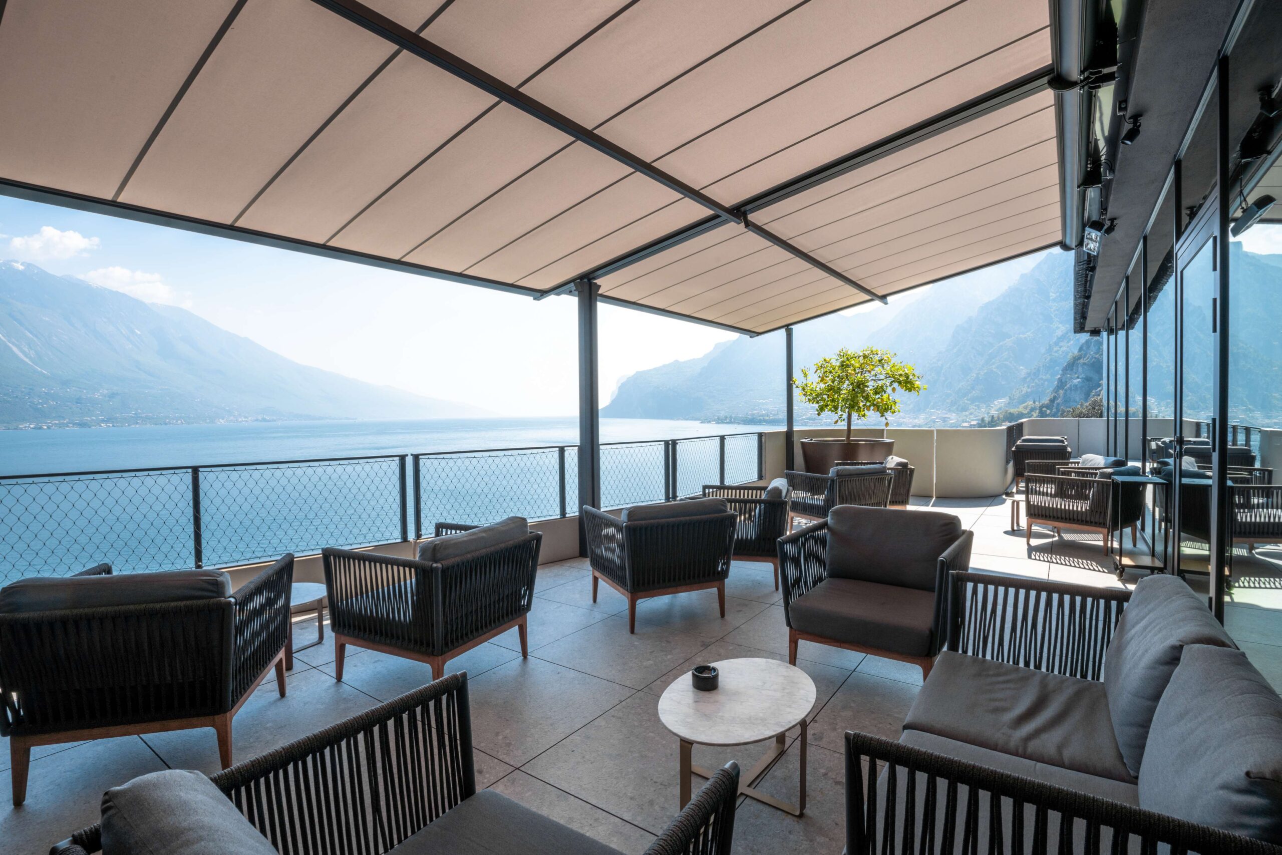 Terrasse avec fauteuils lounge et vue panoramique sur le lac, couverte par un store à toile enroulable ou pergostore.