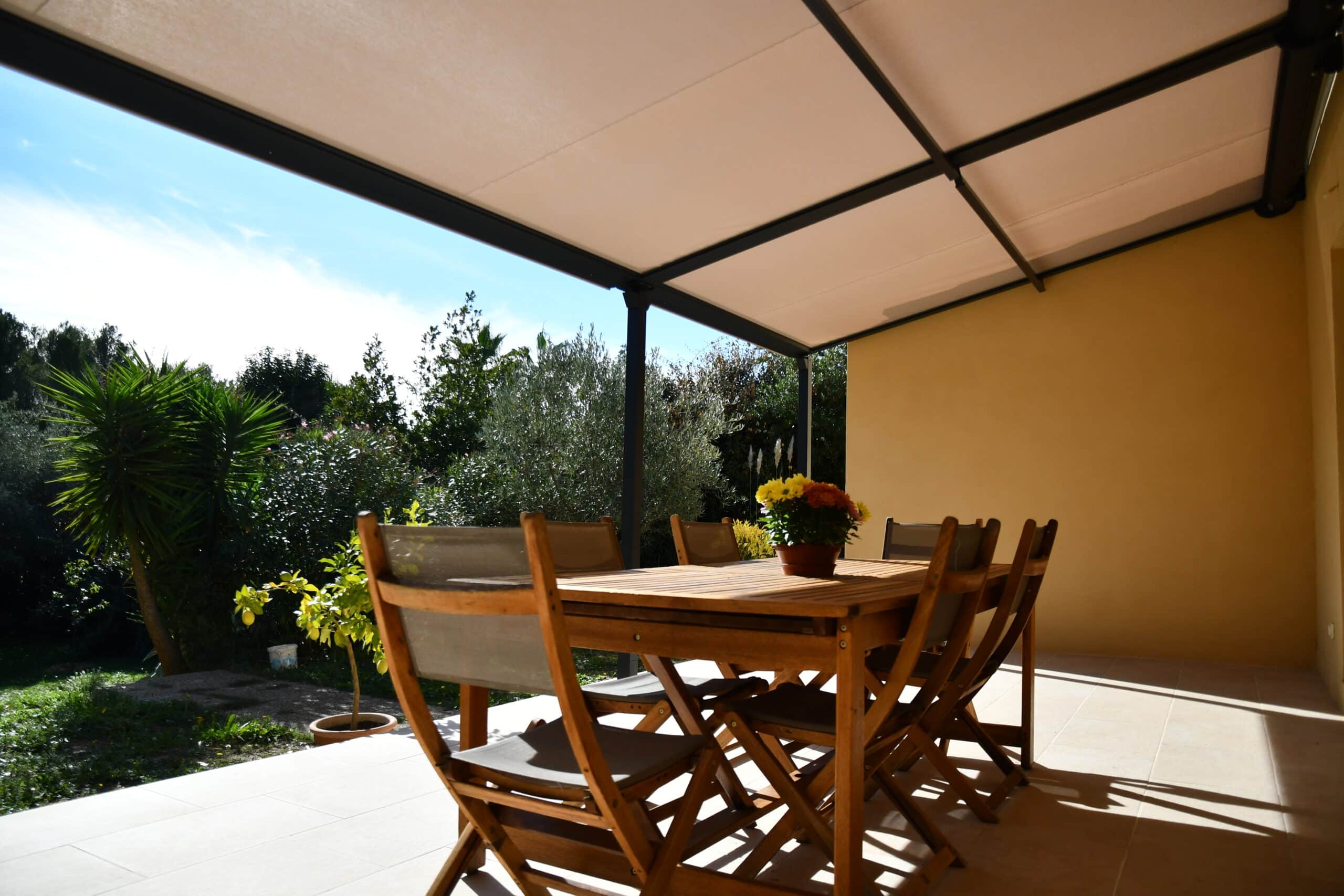 Terrasse ensoleillée avec table en bois et pergola moderne offrant une vue dégagée sur un jardin verdoyant.