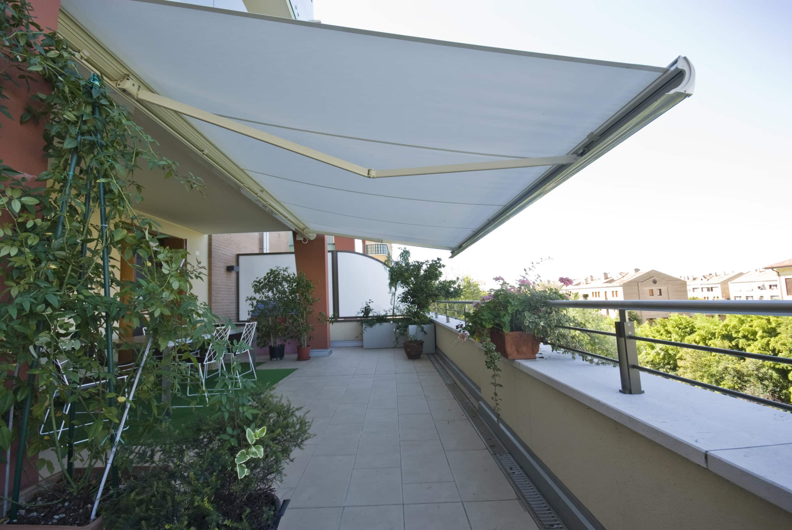 Terrasse ensoleillée avec grand store banne blanc, plantes vertes en pots et vue dégagée sur la ville.