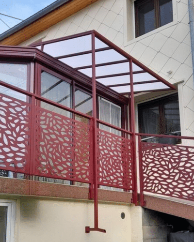 Garde-corps en métal rouge à motifs de feuilles découpés au laser et toit de terrasse assorti sur une maison moderne.