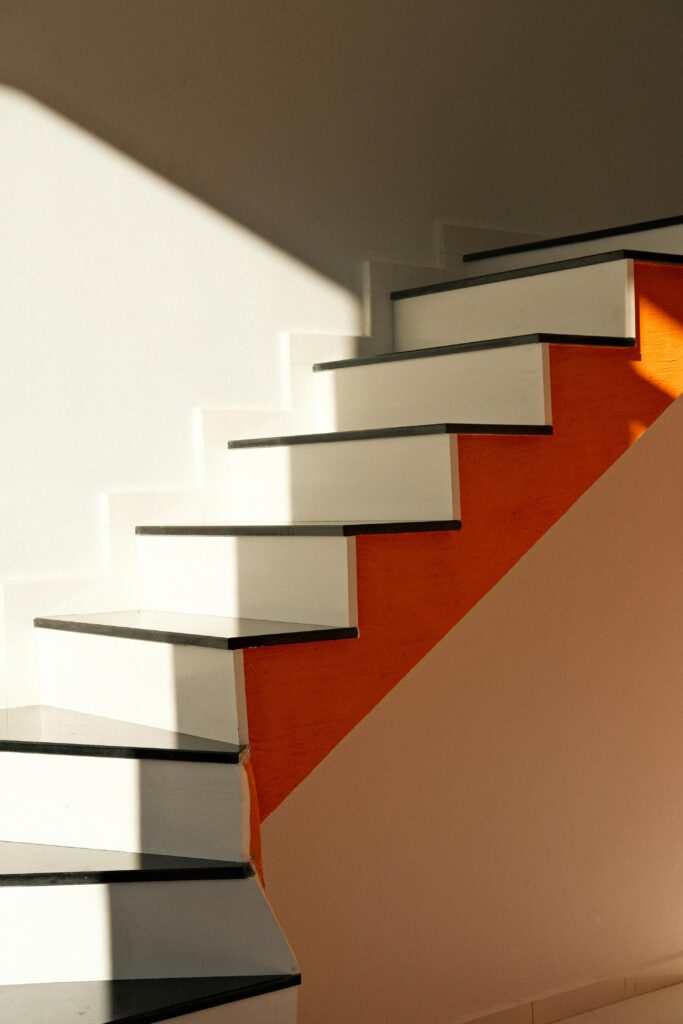 Escalier Minimaliste Moderne avec Mur Orange et Lumière Sunlit white staircase with orange wall and clean lines, showcasing minimalist design.