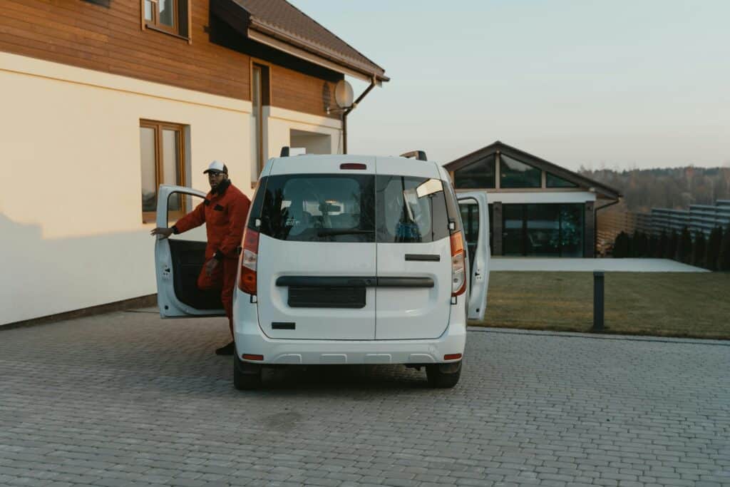 Service de Réparation à Domicile avec Fourgon Blanc A worker in uniform exits a white van parked in a residential driveway during daytime.
