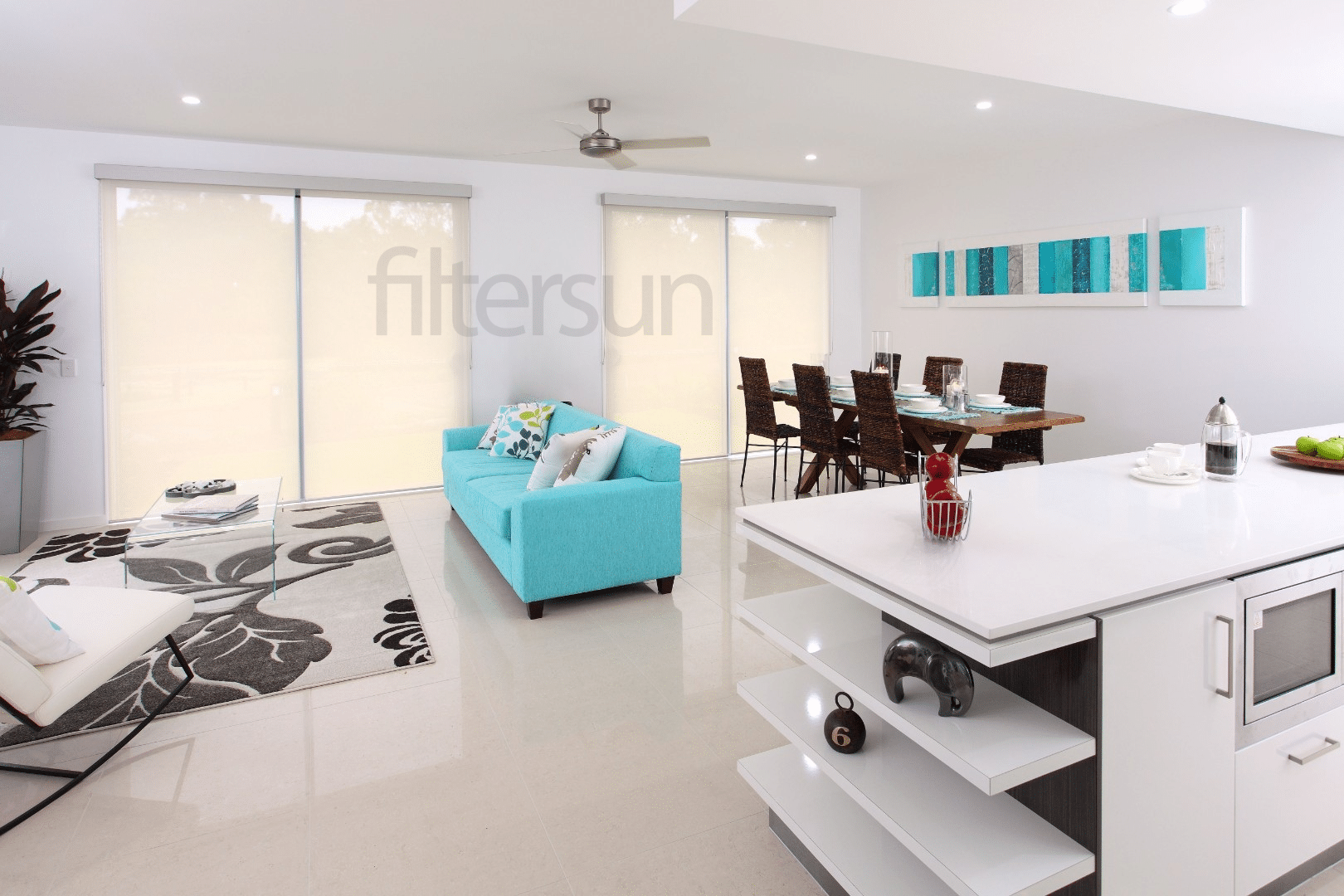 Salon lumineux avec canapé turquoise, salle à manger et stores à enrouleur Filtersun sur baies vitrées.