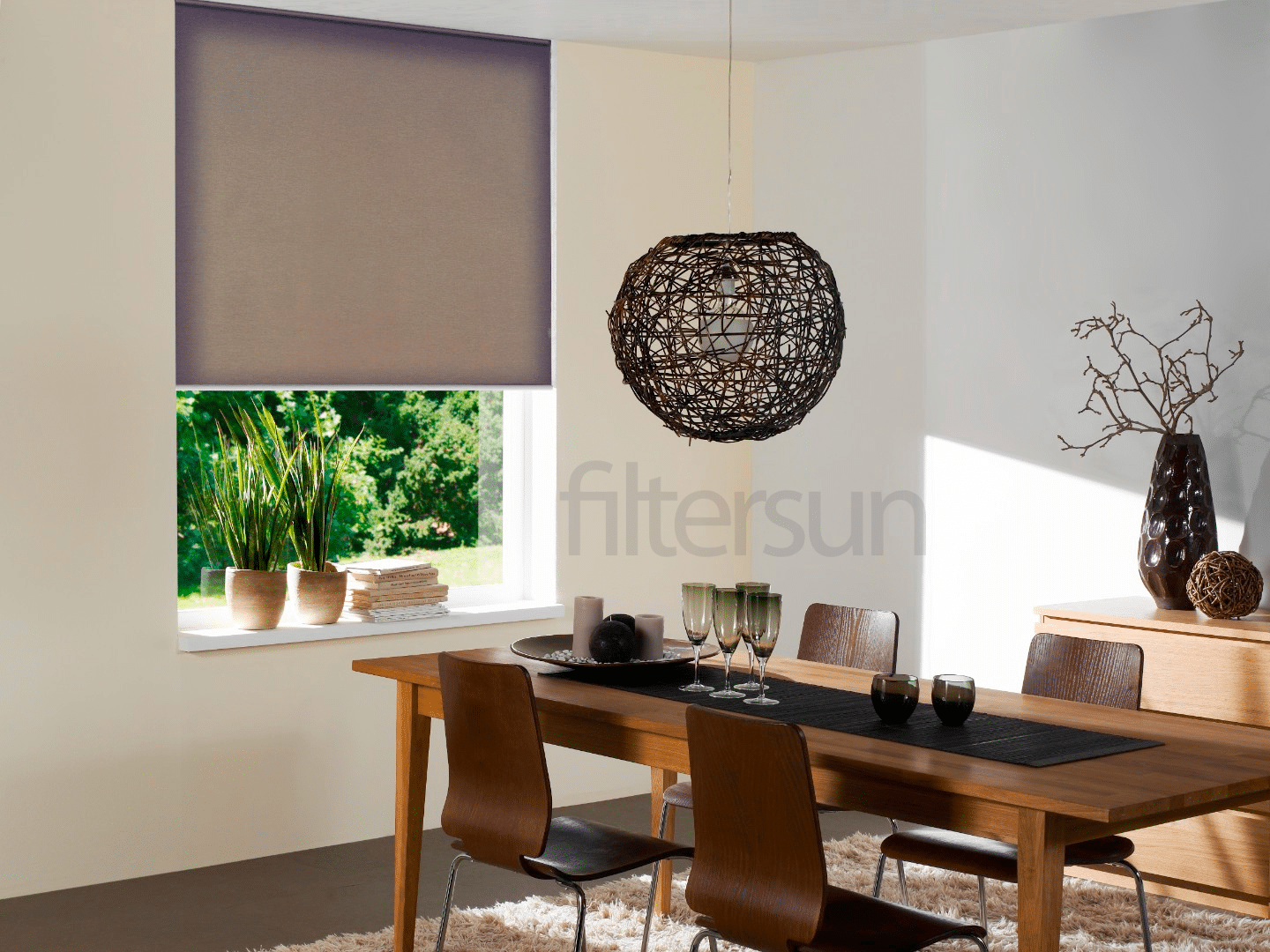 Salle à manger moderne avec store enrouleur gris Filtersun, table en bois et luminaire suspendu en osier.