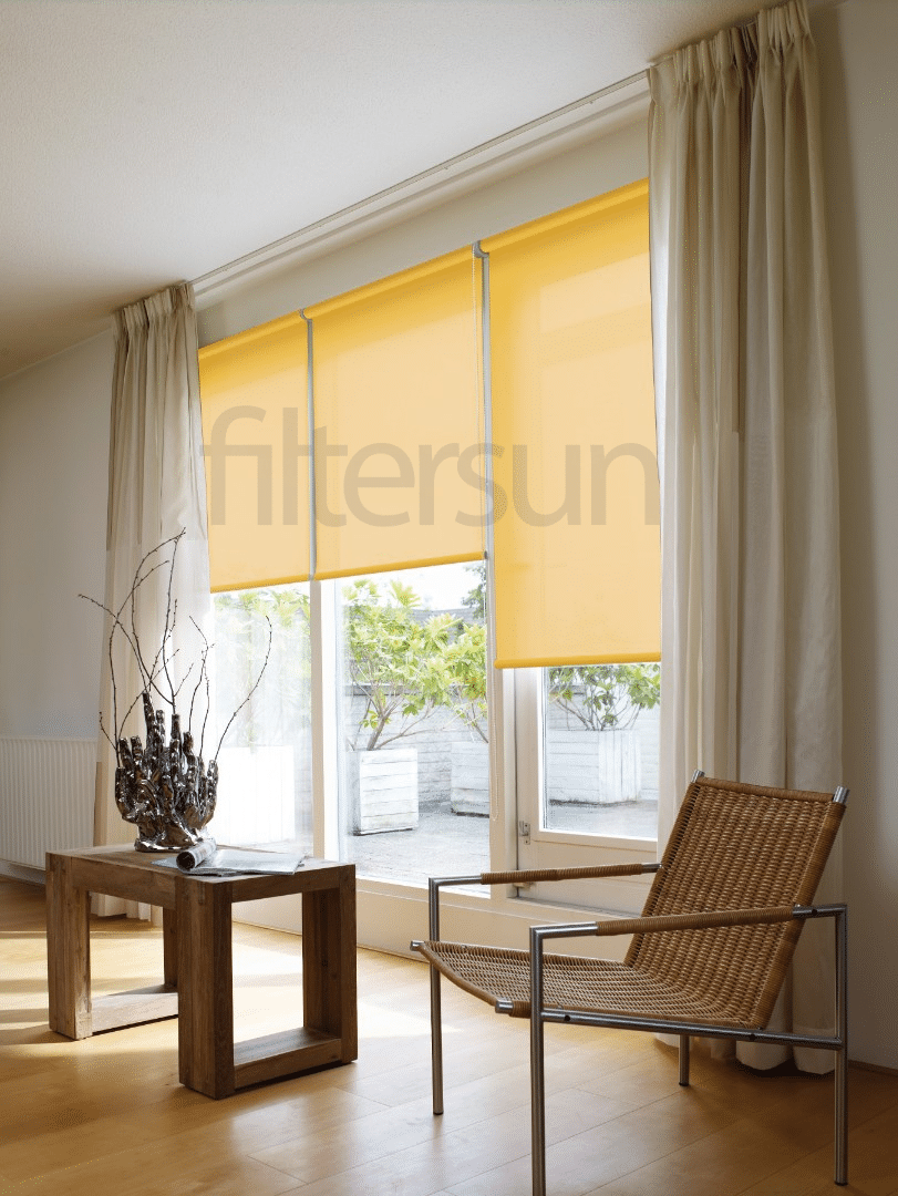 Stores enrouleurs jaunes Filtersun devant une baie vitrée avec rideaux blancs et mobilier design.